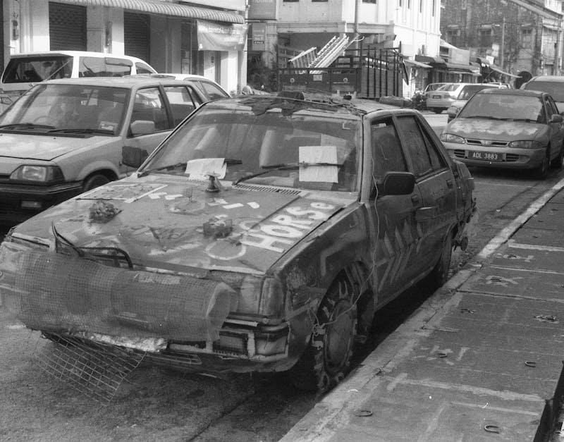 Grayscale image of vandalized cars on an empty street conveying urban decay.