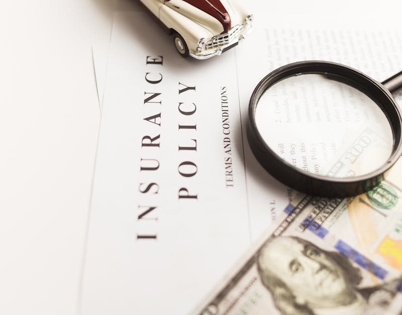 Close-up image of an insurance policy with a magnifying glass, money, and toy car.