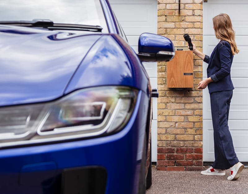 Woman charging an electric car at a home station, promoting sustainability.