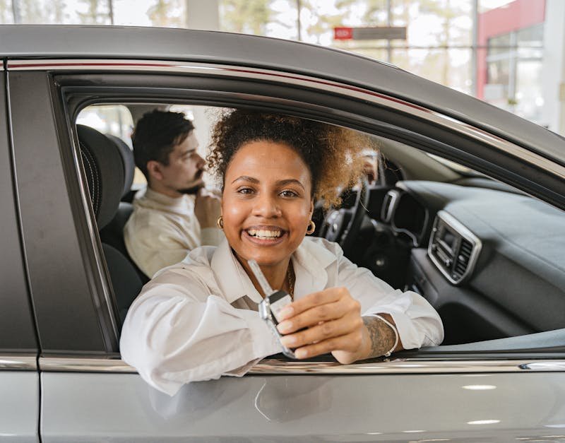 Joyful couple in their new car, holding keys in a dealership showroom, smiling warmly.