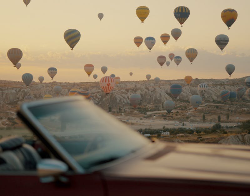 A breathtaking view of hot air balloons floating over Cappadocia's unique landscape at sunrise, captured from a car.