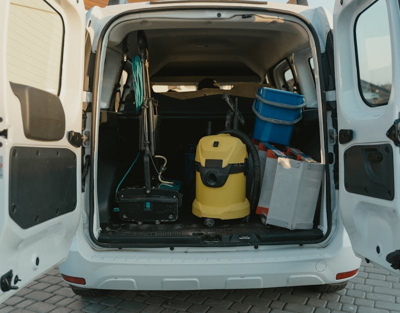 A van with cleaning supplies reveals its open trunk filled with tools and equipment.
