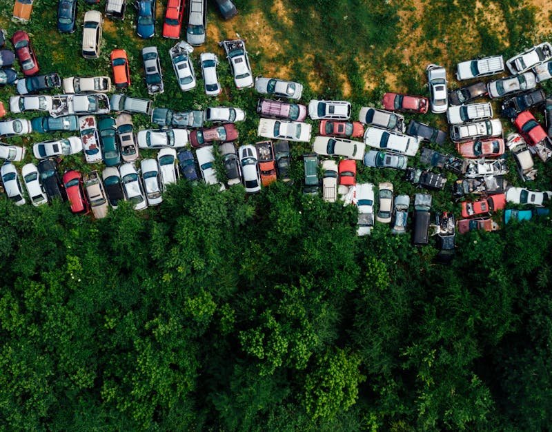 Aerial shot of a junkyard with abandoned cars surrounded by greenery.