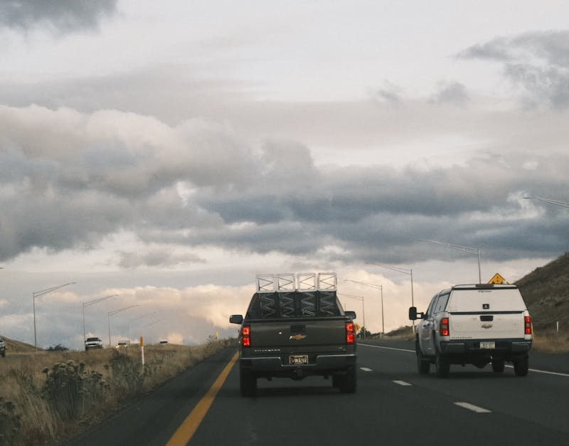 Two pickup trucks drive along a scenic highway under cloudy skies.