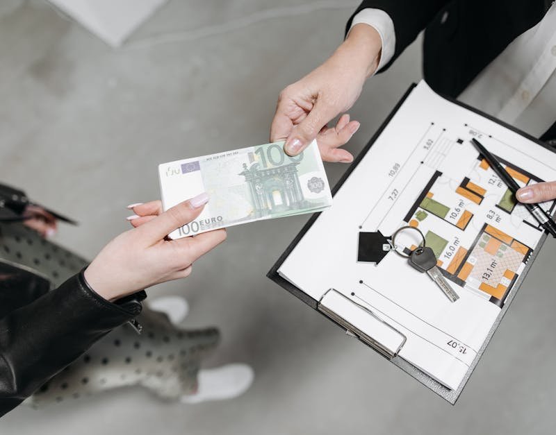 Close-up of a real estate transaction with euro bill, keys, and floor plan.