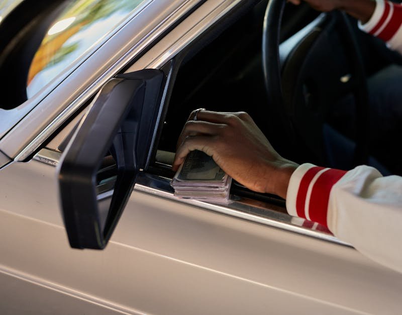 A close-up view of a hand holding cash through a car window, capturing a candid moment.