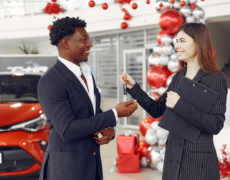 A car dealer handing over keys to a satisfied customer at a decorated dealership.