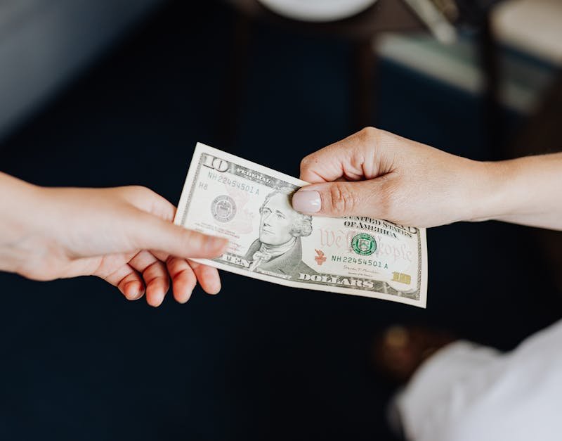 Two people exchanging a ten dollar bill in a close-up hand-to-hand transaction.