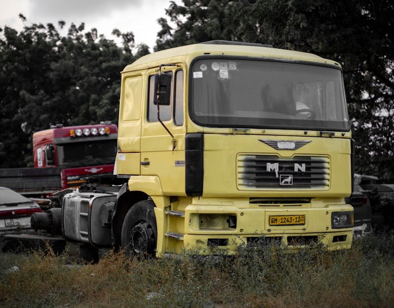 A yellow truck cab parked in an outdoor lot surrounded by other vehicles and trees.