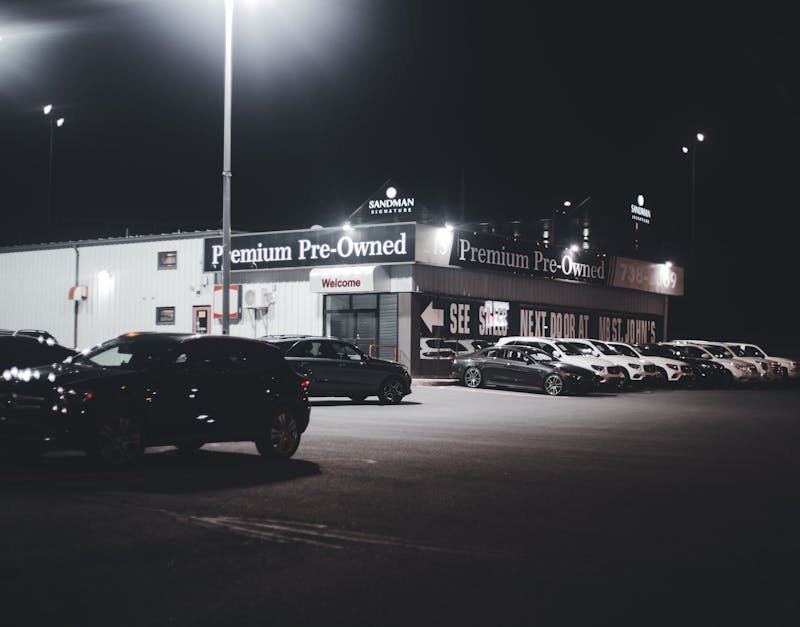 Illuminated car dealership lot showcasing premium pre-owned vehicles at night.