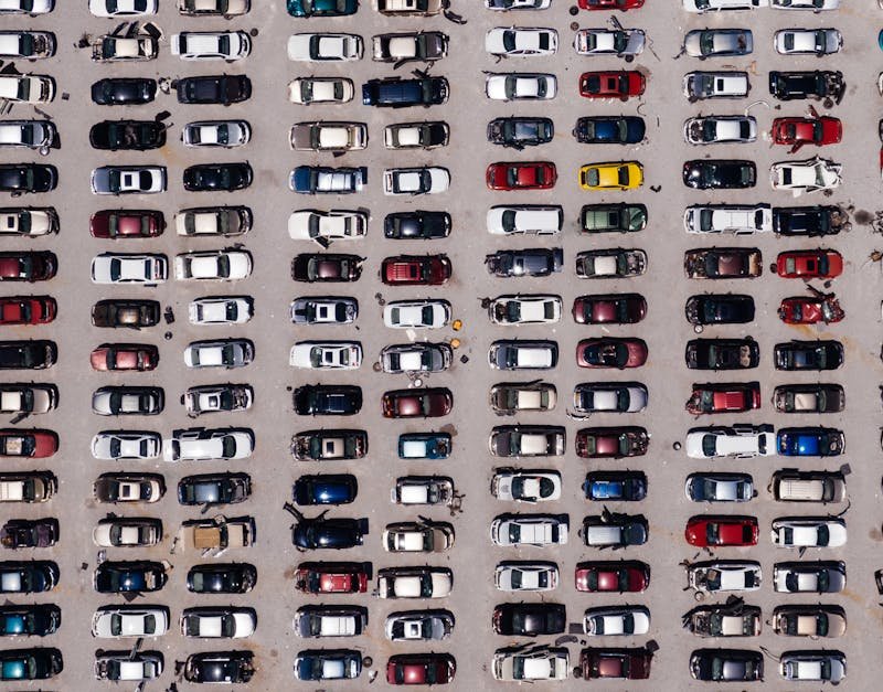 Top-down aerial shot of a large parking lot filled with rows of cars, showcasing organized symmetry.