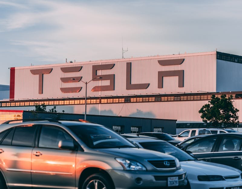 Tesla factory with parked cars during sunset, showcasing modern automotive industry vibes.