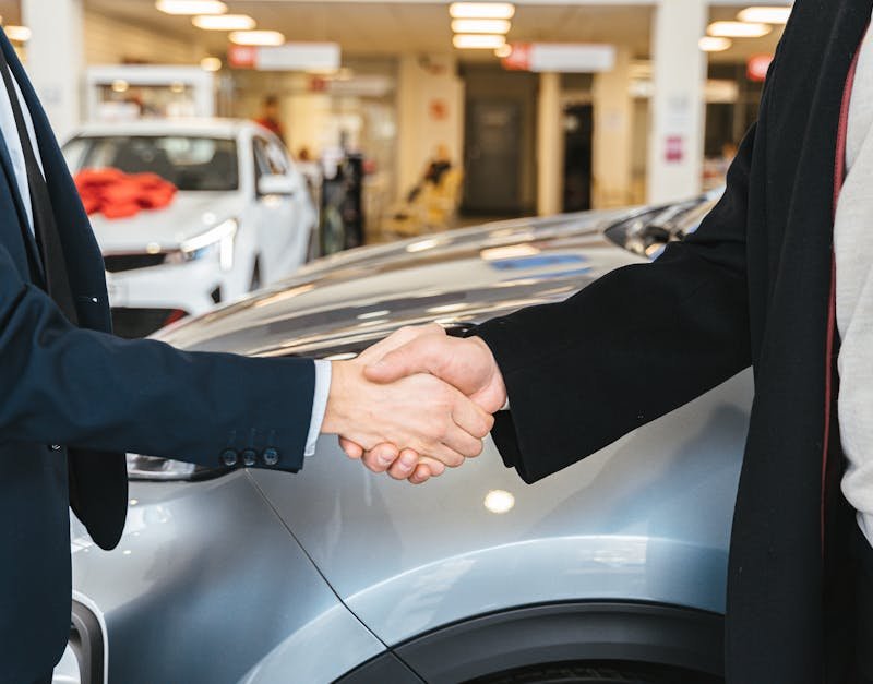 Two businessmen shaking hands in a car dealership, sealing a deal.