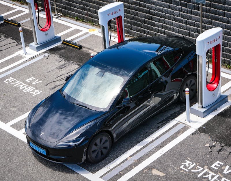 A black Tesla parked at a charging station in an urban setting.