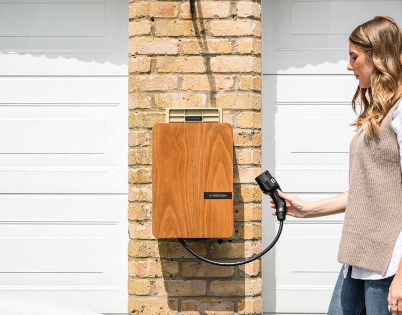 A woman uses a home electric vehicle charger mounted on a brick wall.