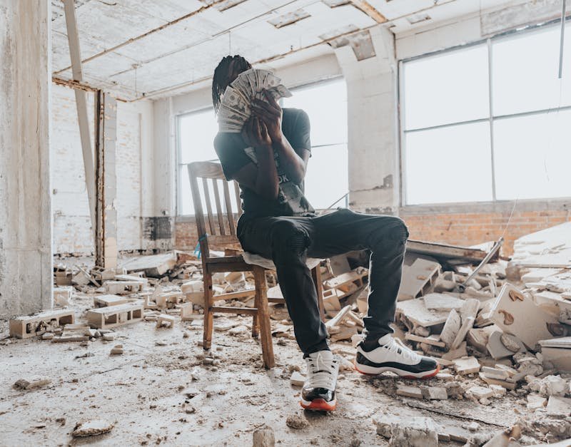 A person sitting on a chair in a dilapidated building holding a stack of cash.