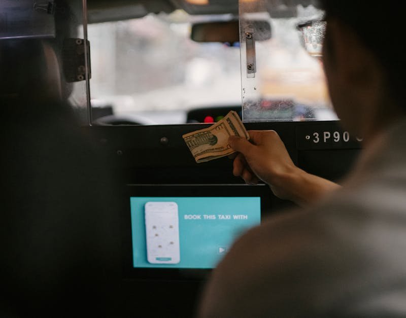 Back view of taxi car interior with tablet screen located near passenger seat and client paying for ride