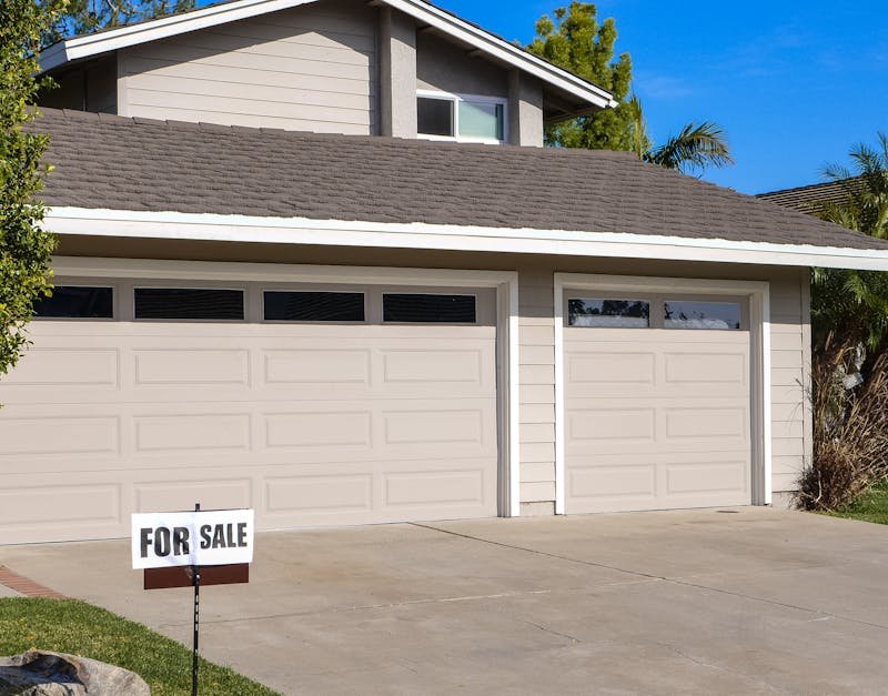 Modern residential house with a two-car garage and a for sale sign.