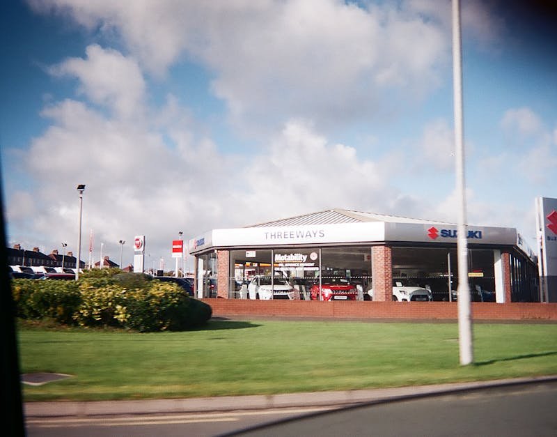 Exterior view of a car dealership featuring Suzuki automobiles under a bright sky.