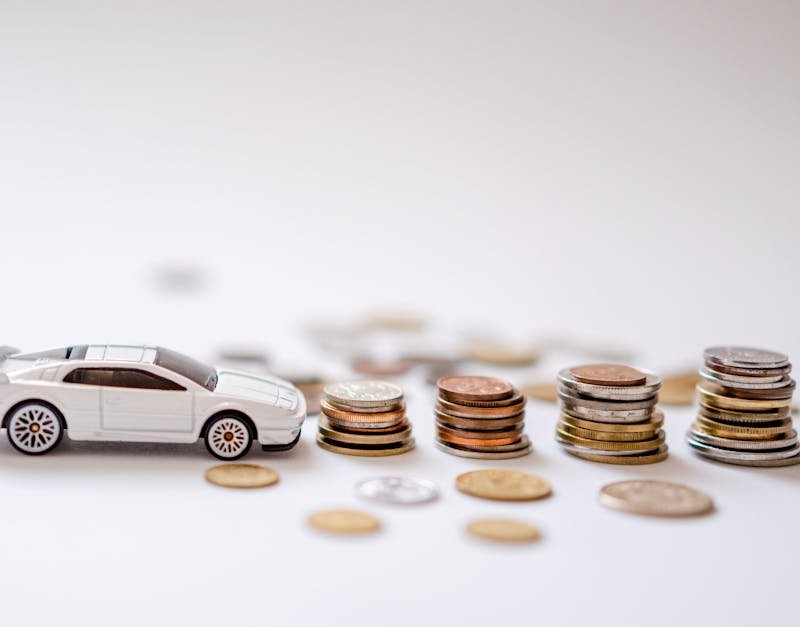 White toy sports car beside stacks of coins on a white background, emphasizing savings and finance.