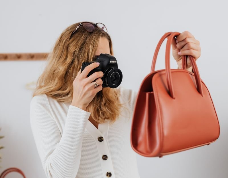 A woman in white long sleeves photographs a handbag, ideal for online selling and fashion themes.