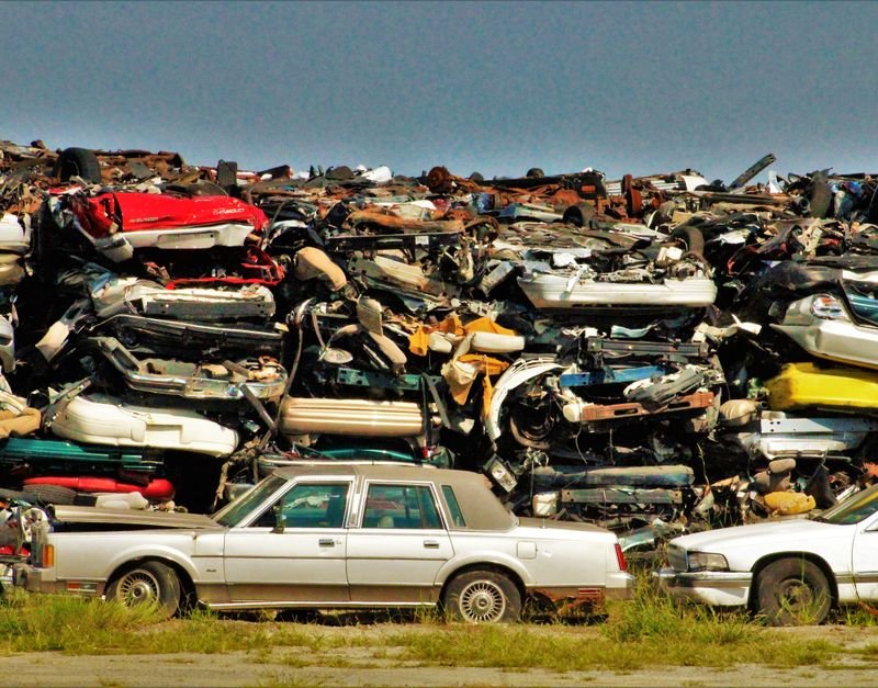 A large stack of disposed vehicles in an outdoor junkyard.