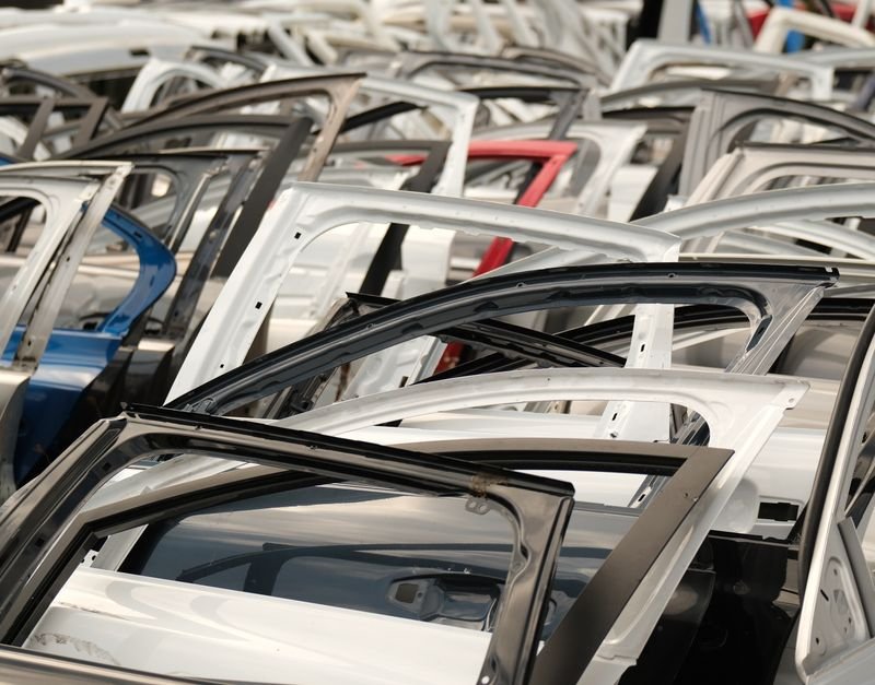 A variety of car doors in different colors arranged in a junkyard setting.